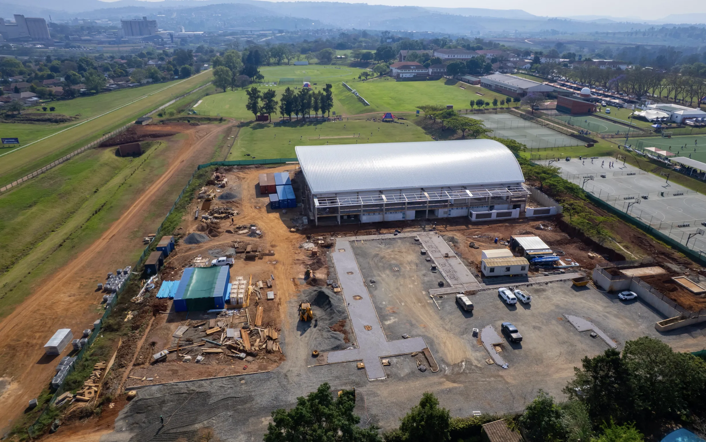 Exterior view of AquaPark facility with parking area in front, main enclosed pool building and adjacent landscaped grounds under a blue sky in Pietermaritzburg.